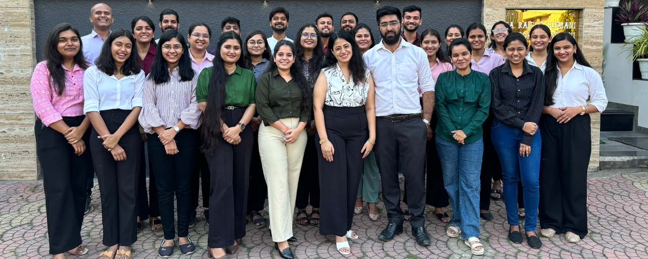 A group of people, representing the best outsourced accounting company in the USA, pose together in front of a building. They are smiling and dressed in business or casual attire. The setting appears to be outdoors with a stone pavement.