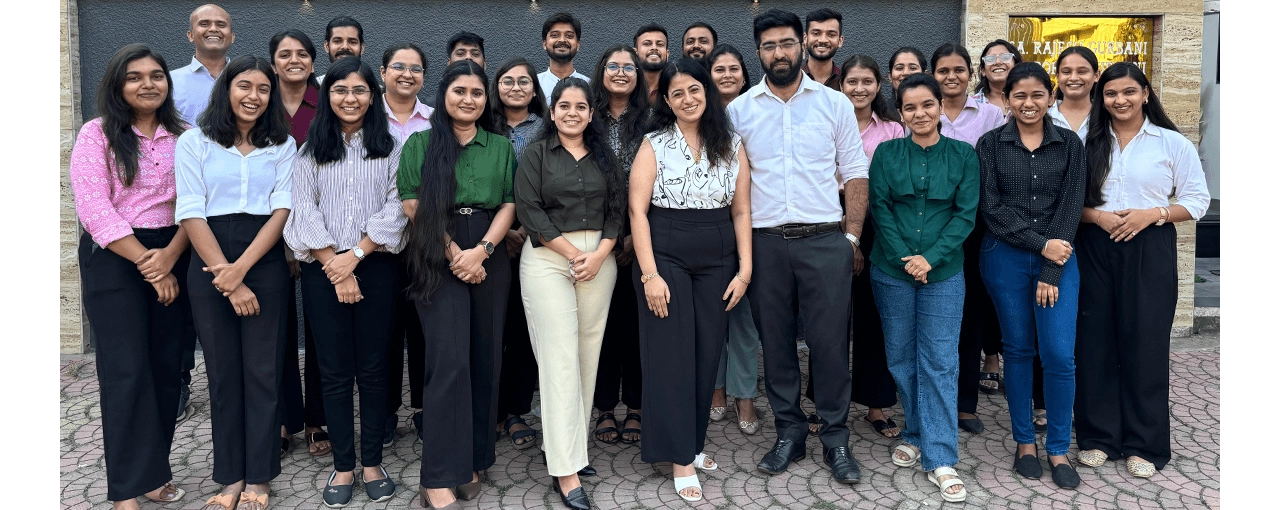 A group of people, representing the best outsourced accounting company in the USA, pose together in front of a building. They are smiling and dressed in business or casual attire. The setting appears to be outdoors with a stone pavement.